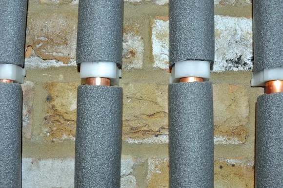 Isolierte Heizungsrohre an einer Ziegelwand